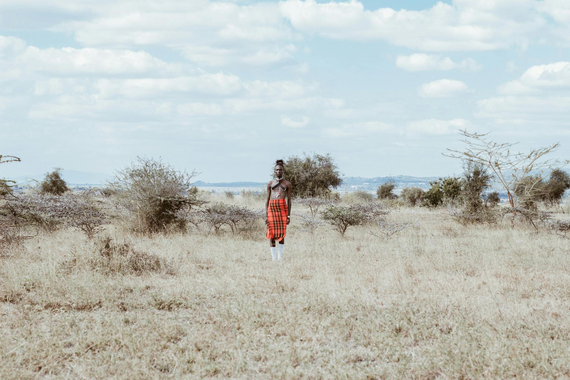 photo of man in red and white lungi skirt standing on grass field